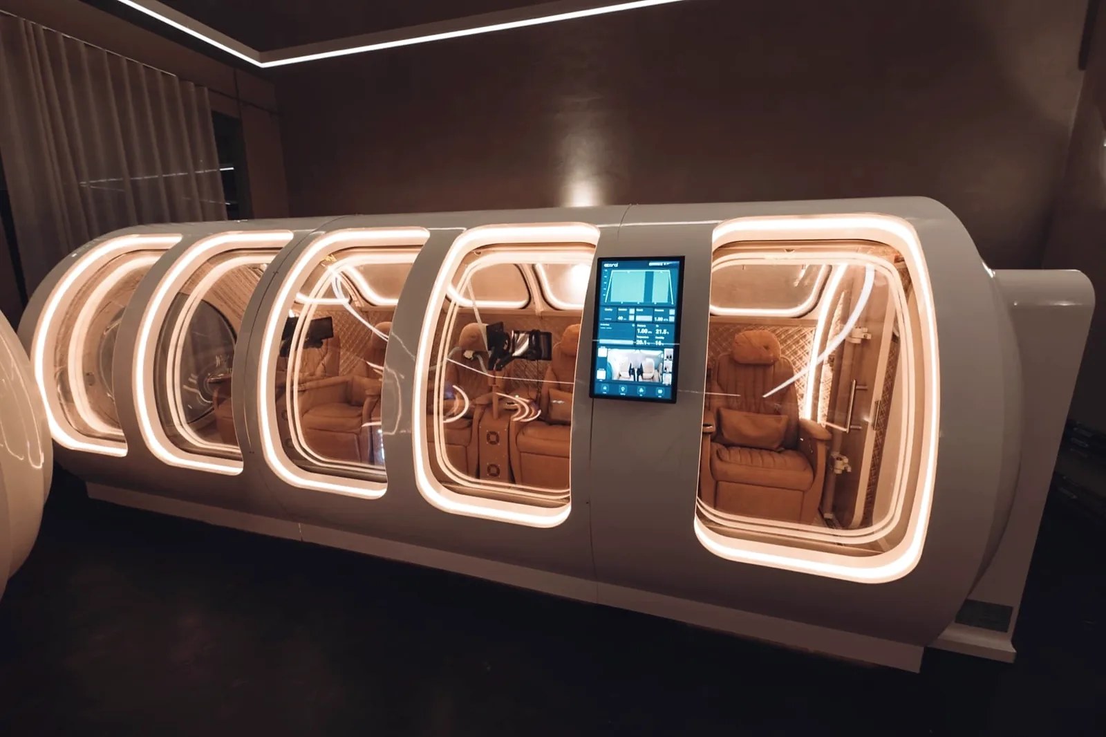 La cámara hiperbárica con forma de omega de Age Back Clinic Stockholm, con los asientos interiores iluminados visibles a través de las ventanas del recipiente de presión